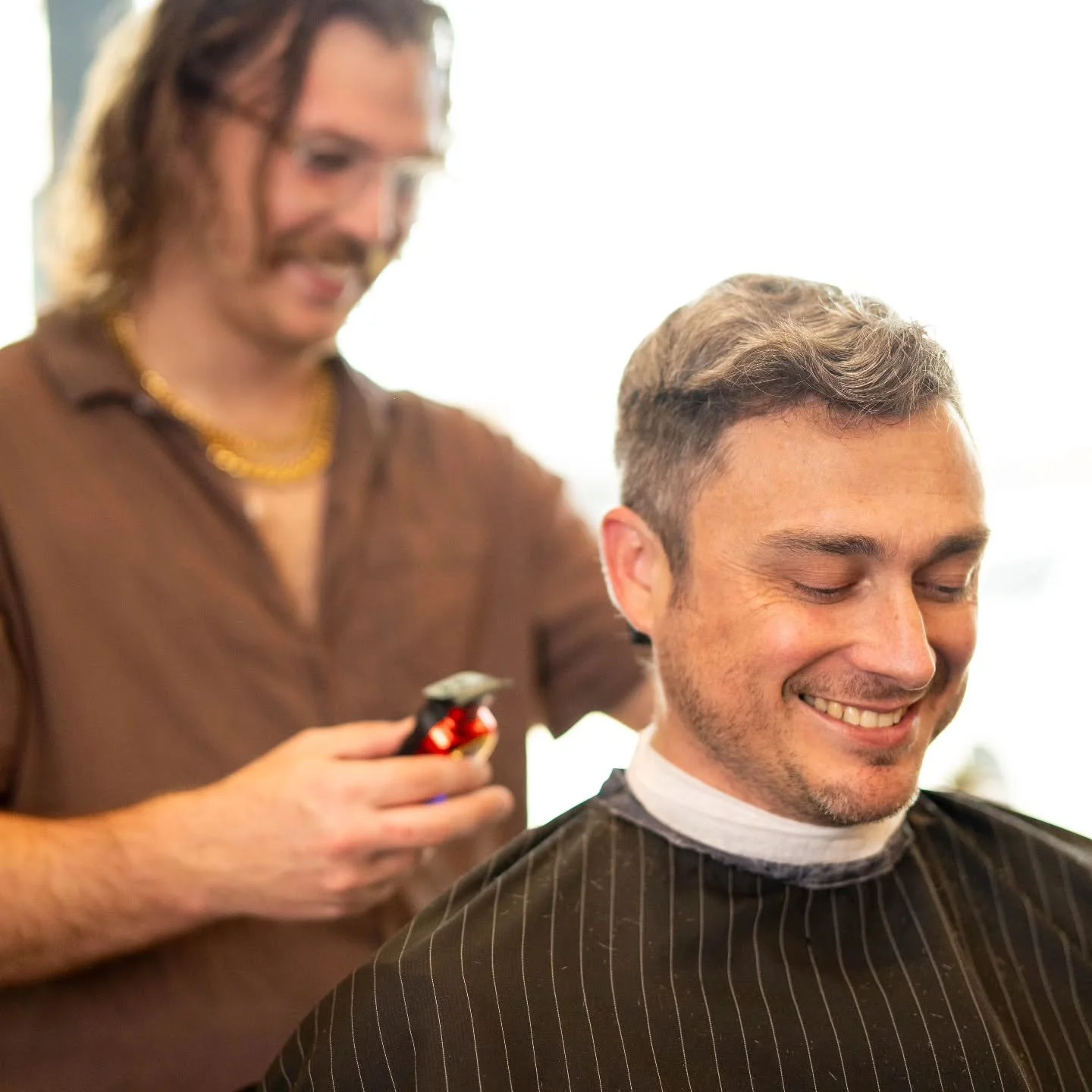 Barber holding a red trimmer behind a smiling client with a short textured haircut.