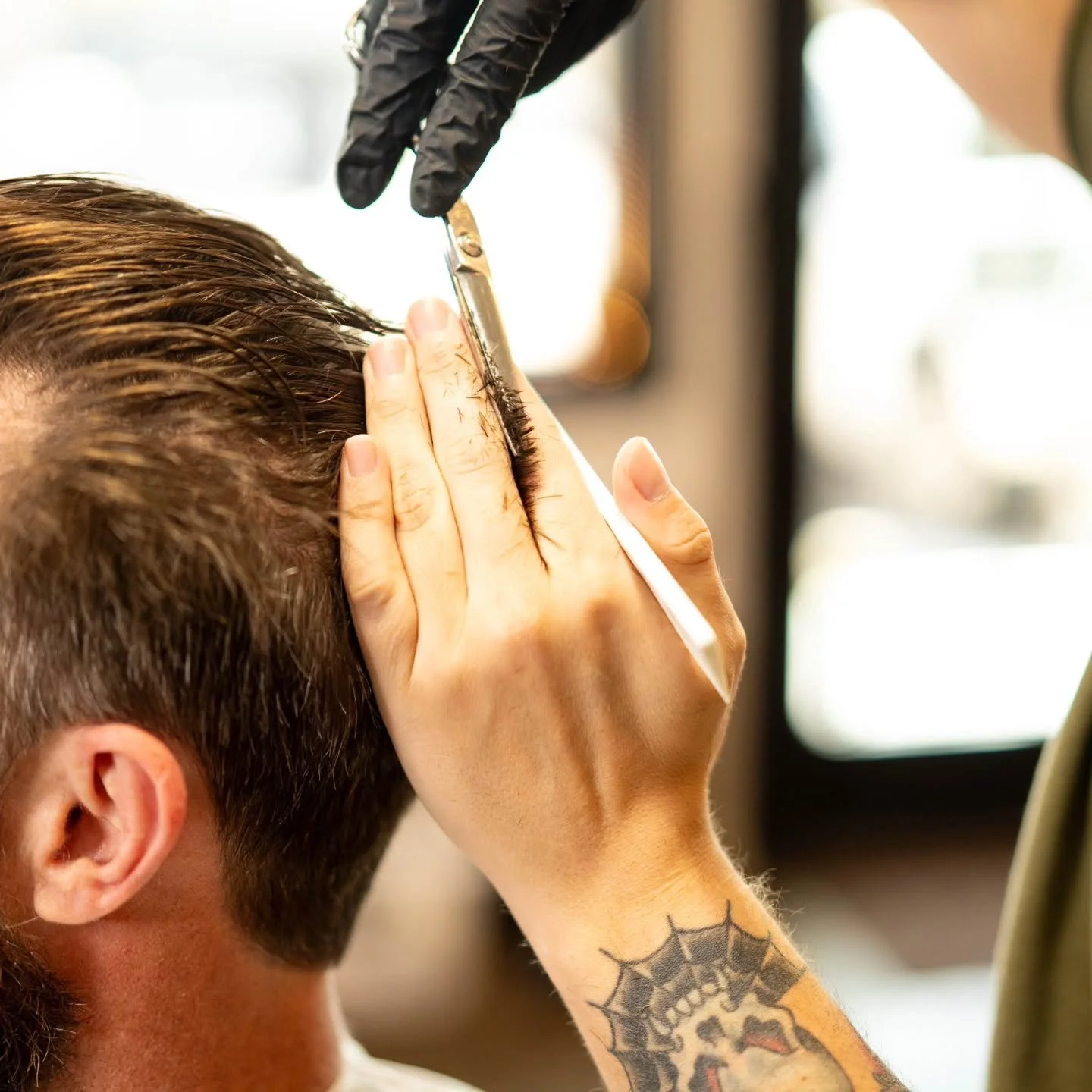 Barber using scissors and a comb to shape hair along the side of a client's head.