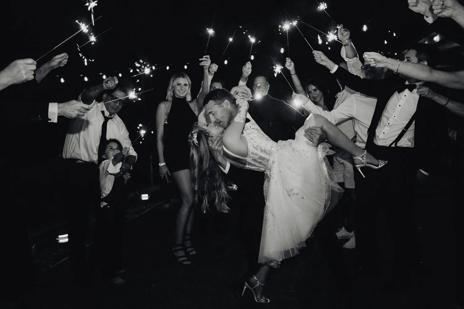 Wedding guests holding sparklers form a tunnel as the bride is carried through at the end of a Los Angeles reception