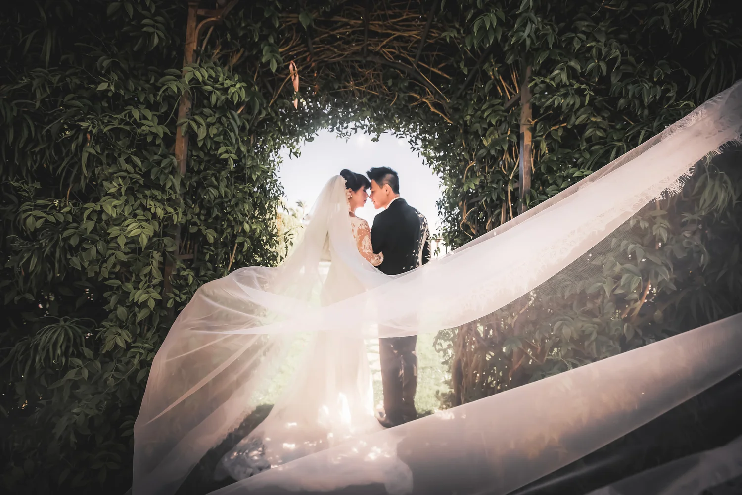 A couple under a backlit leafy arch at a Vietnamese wedding in Southern California