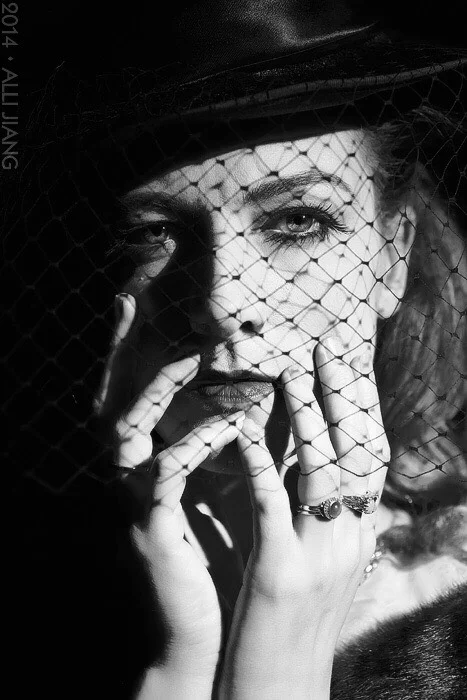 Black and white glamour portrait with a birdcage veil and vintage hat