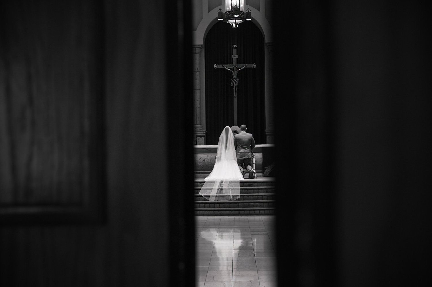 Bride walking toward a lit altar down a dark church aisle, photographed in black and white by Lulan Studio