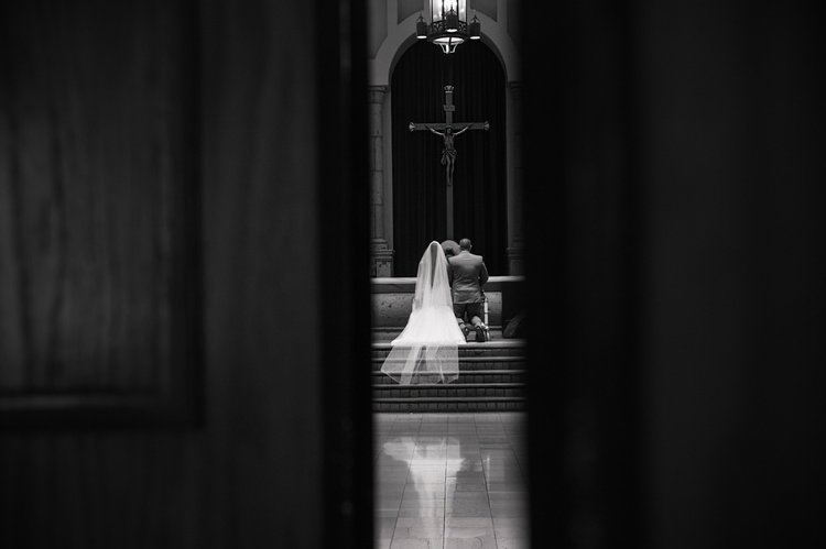 Bride walking toward a lit altar down a dark church aisle, photographed in black and white by Lulan Studio