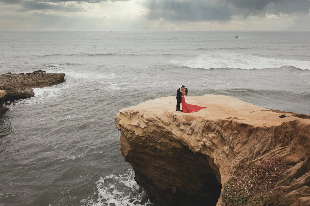 Couple standing on a sandstone bluff above the Pacific during a coastal engagement session
