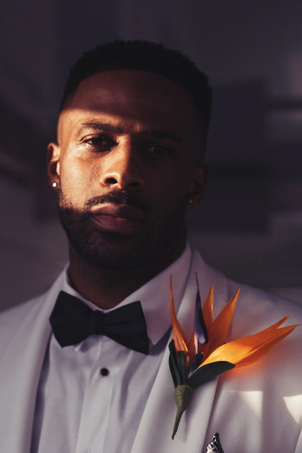 Groom in a white tuxedo jacket and black bow tie with a bird of paradise boutonniere