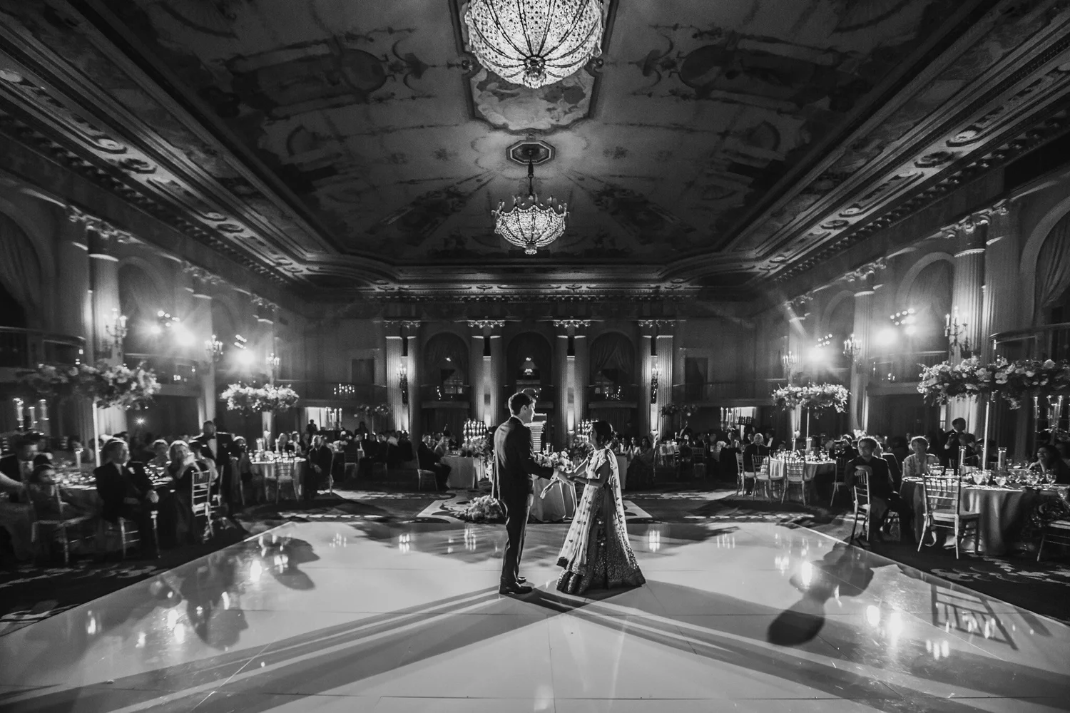 Black and white frame of a first dance in the middle of a grand ballroom, guests seated around the floor