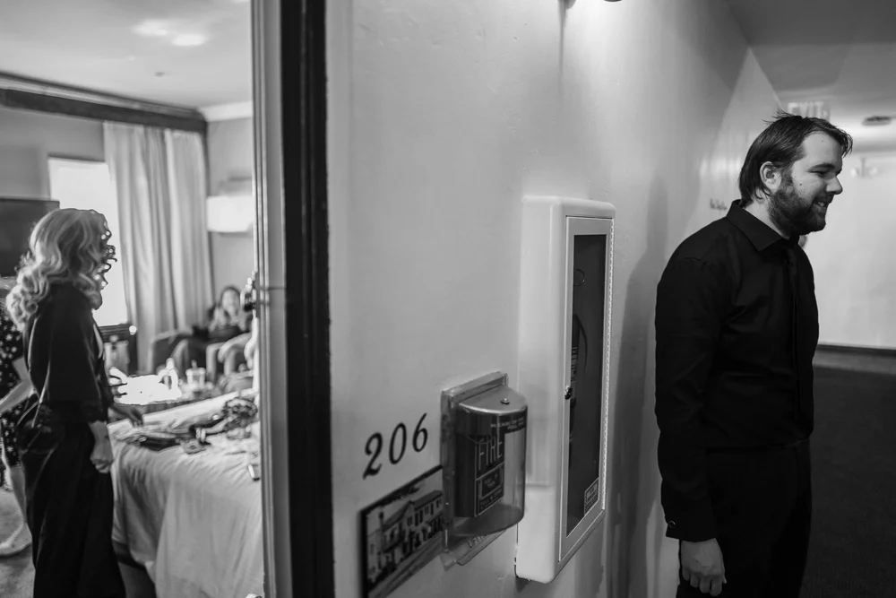 Groom waiting in a hotel corridor outside room 206 before the first look, black and white