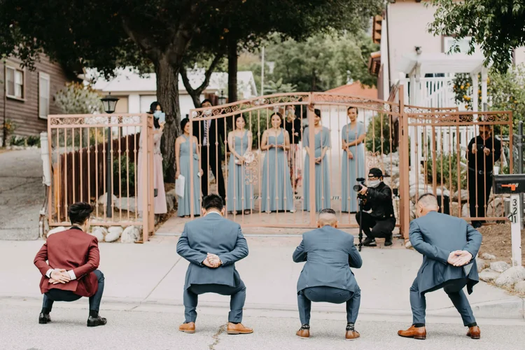 A large wedding party at an outdoor ceremony, groomsmen seated and bridesmaids in blue standing behind
