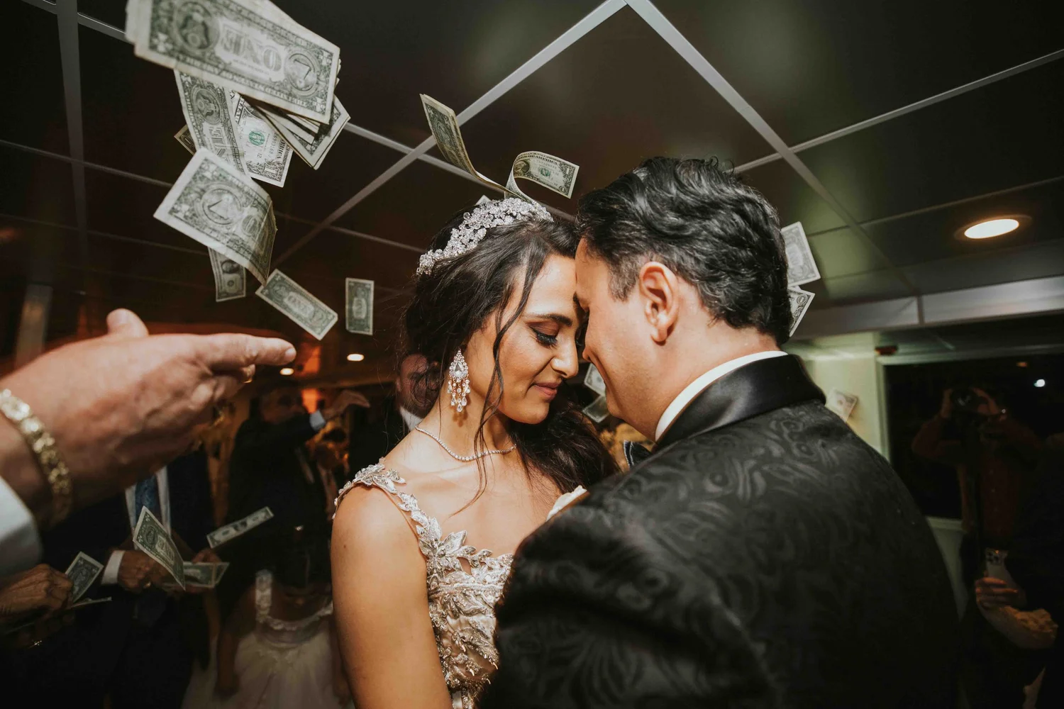 Bride and groom forehead to forehead as dollar bills fall around them during a money dance