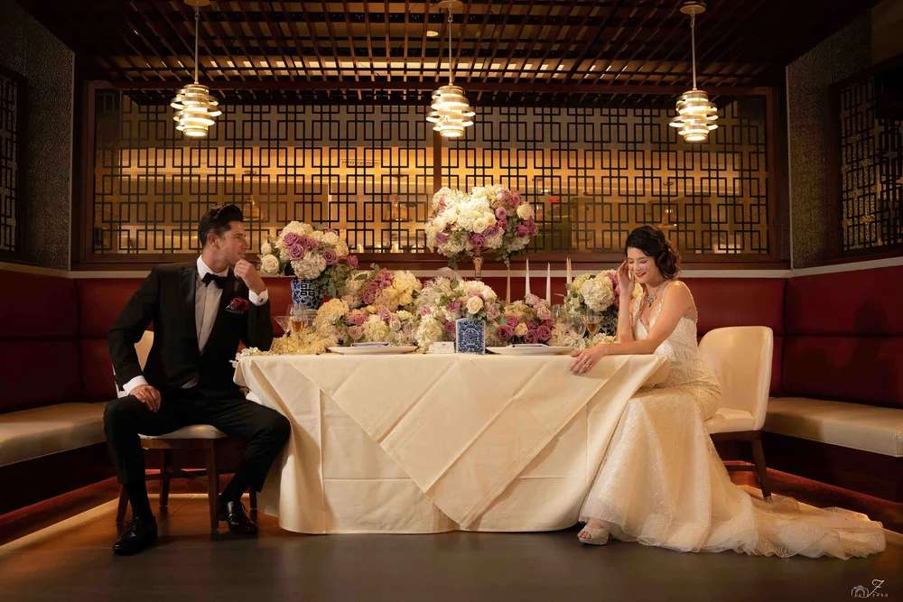 Bride and groom at a flower-covered sweetheart table beneath pendant lamps