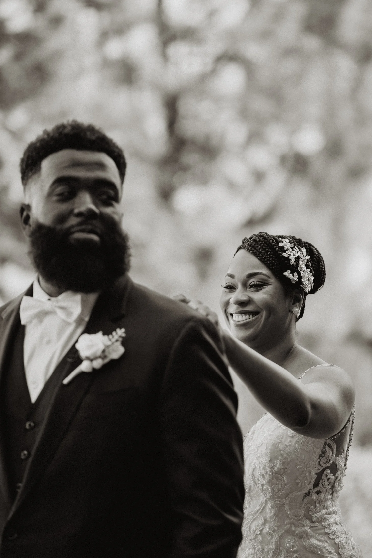 Black and white frame of a bride adjusting the groom’s lapel, both smiling