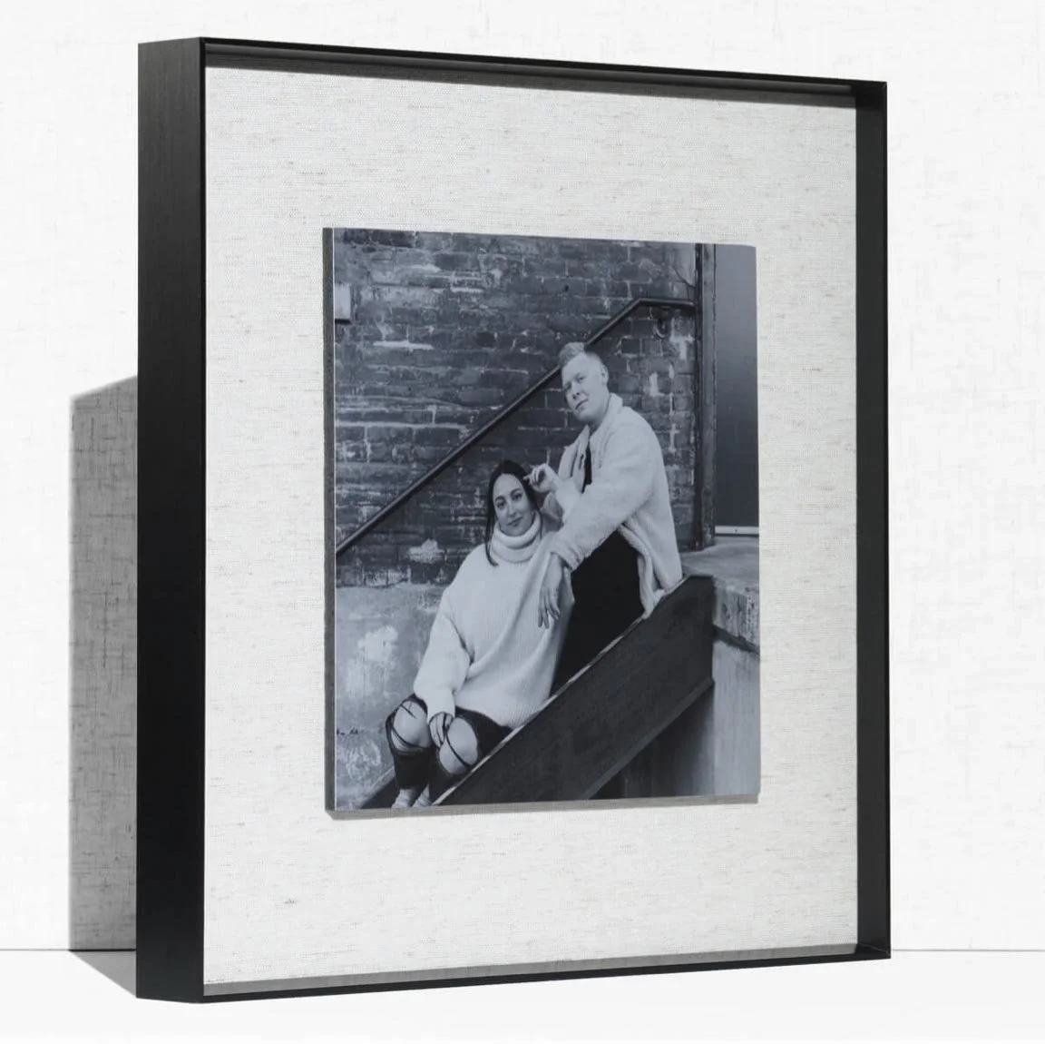 Black metal float frame holding a black-and-white portrait of a couple on a linen backdrop