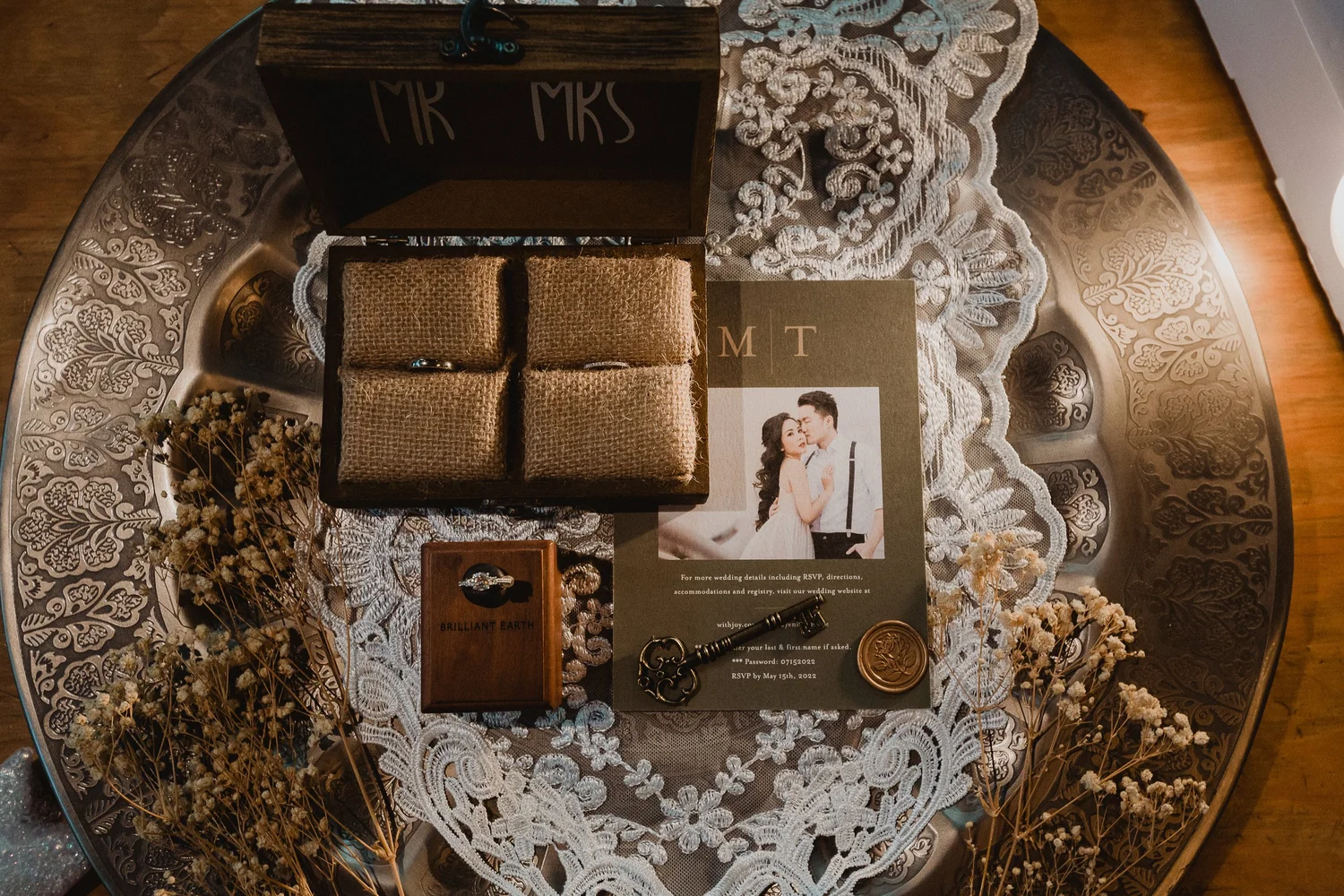 Wedding flat lay of ring boxes, an invitation and antique lace on a silver tray