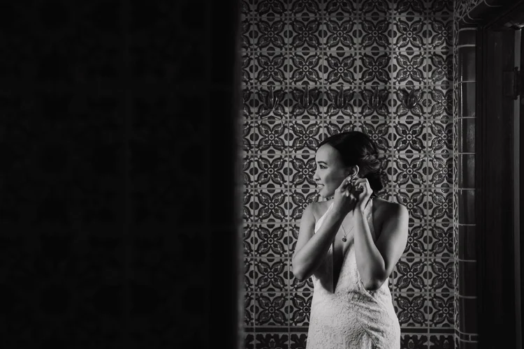 Black-and-white photo of the bride fastening an earring against a patterned tile wall before Helena and Kerry's wedding at Adamson House in Malibu