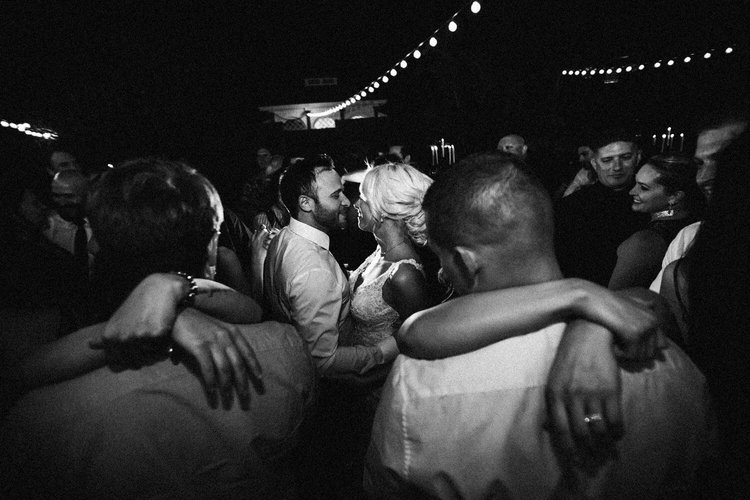 Couple kissing in the middle of a crowded dance floor with all their guests around them, black and white
