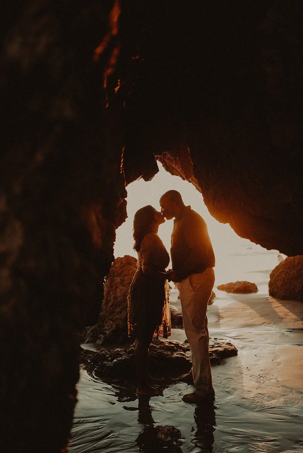 Couple kissing inside a sea cave at sunset