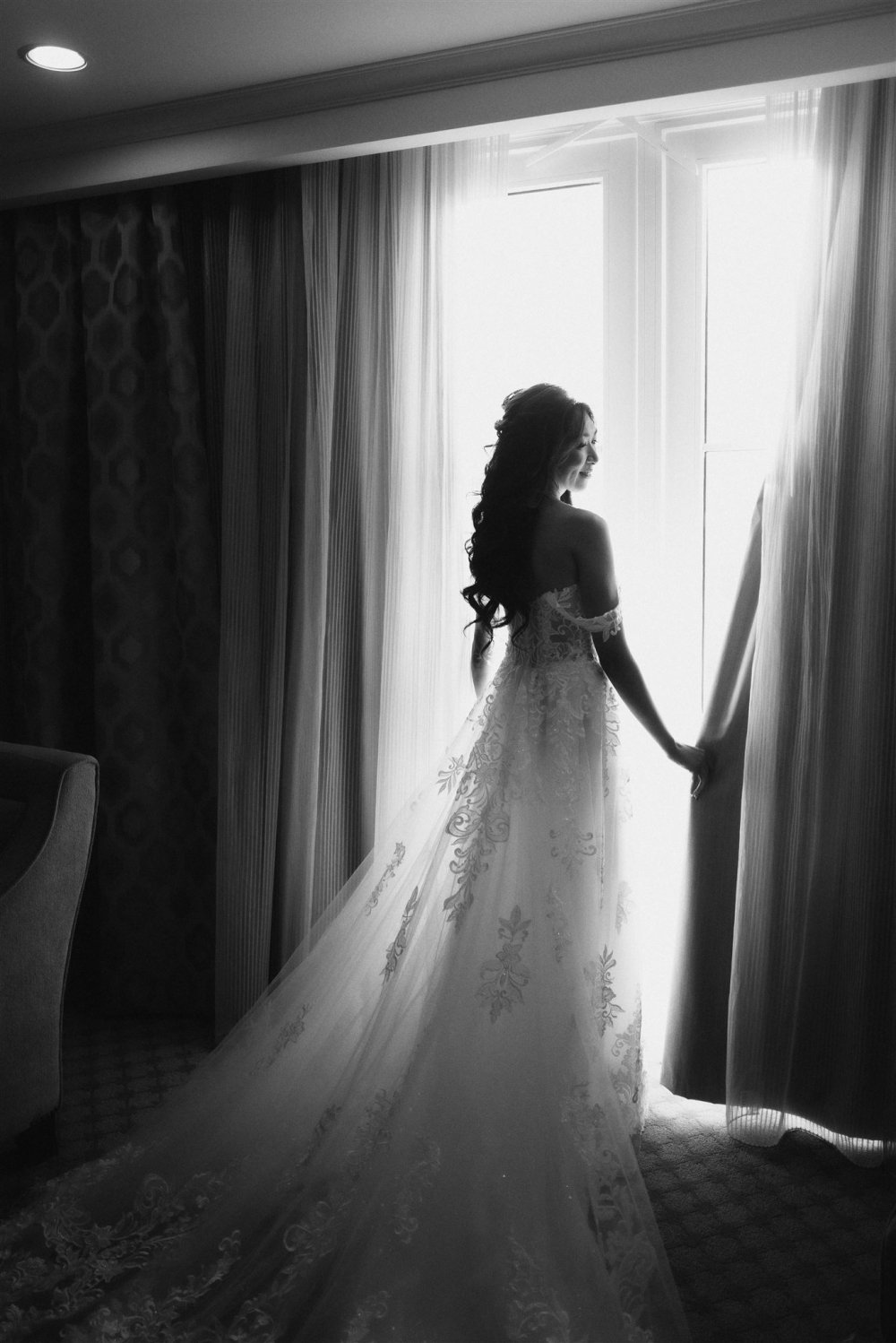 A bride standing at a bright hotel window in black and white, photographed on 35mm film with available light only