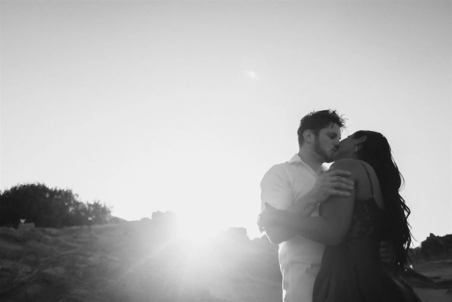 A couple kissing against a blazing low sun, photographed on black and white 35mm film with a Leica rangefinder