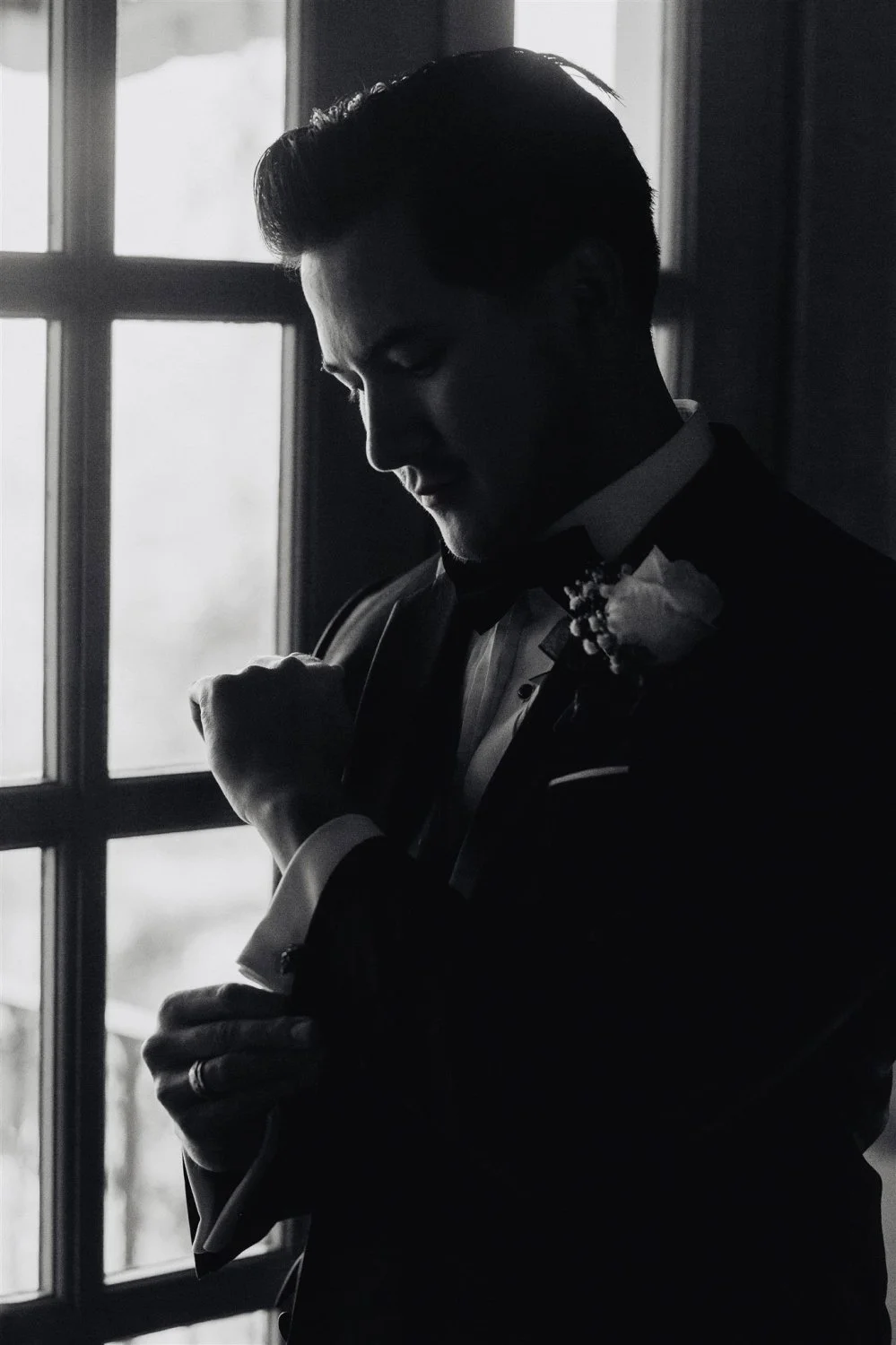 Groom fastening his jacket beside a window in low light