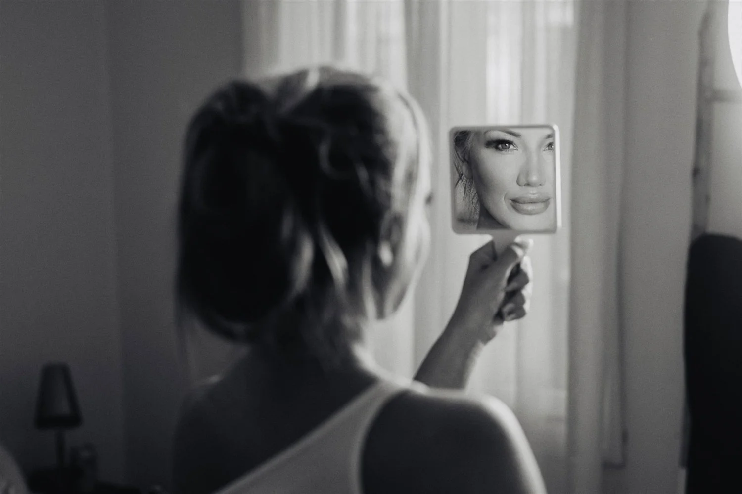 Black and white frame of a bride checking her reflection in a small handheld mirror