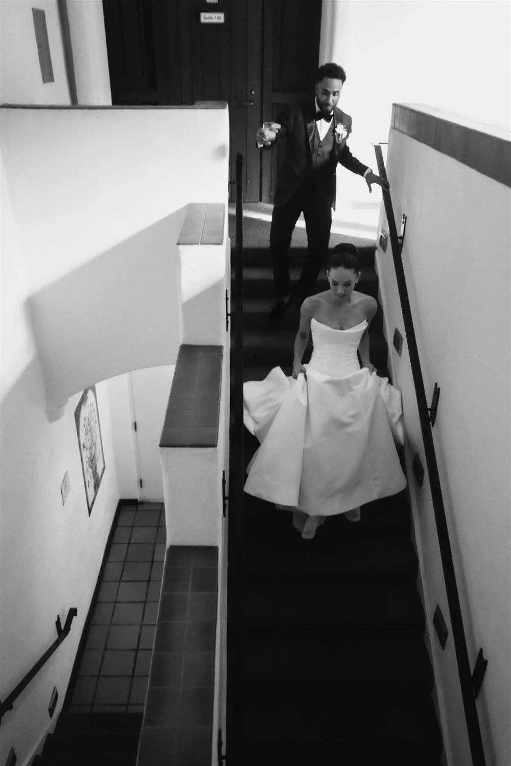 Groom watching from the top of a stairwell as the bride climbs toward him