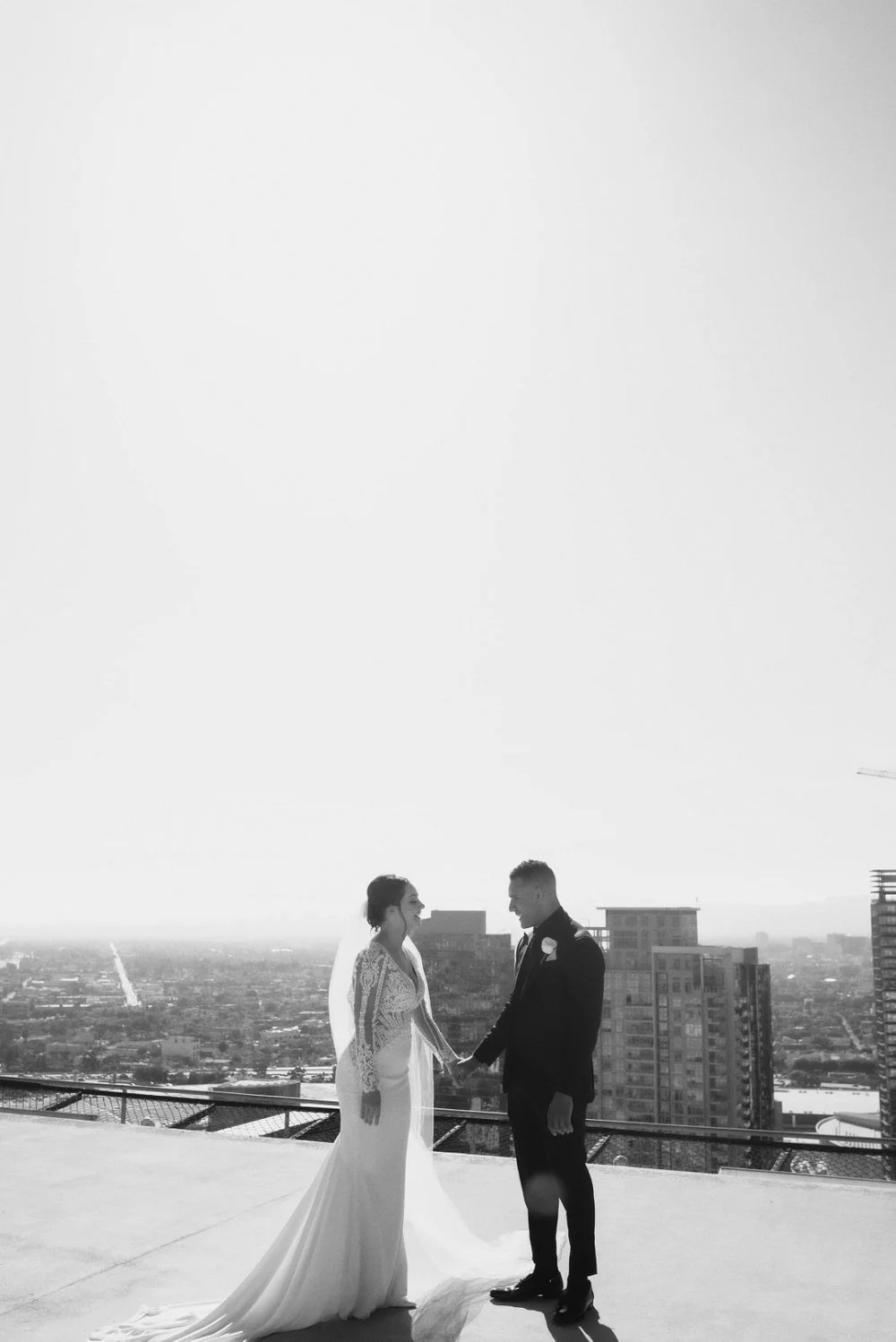 Bride and groom on a rooftop under a white sky, the city spread out below