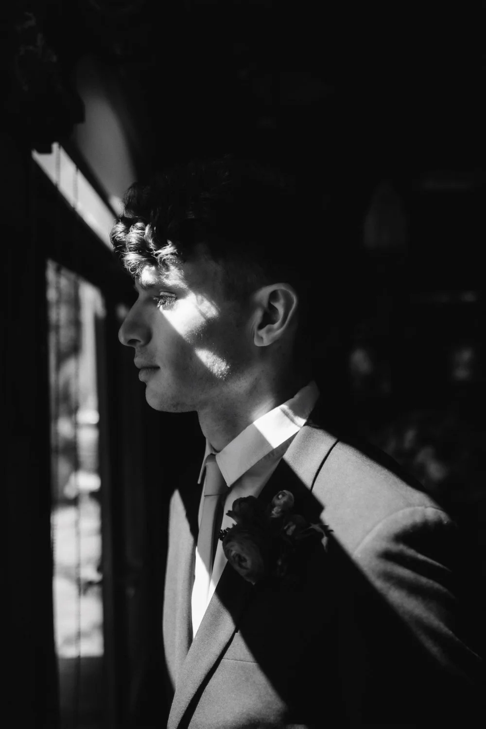 A shaft of window light falling across a groom’s face, photographed on black and white film