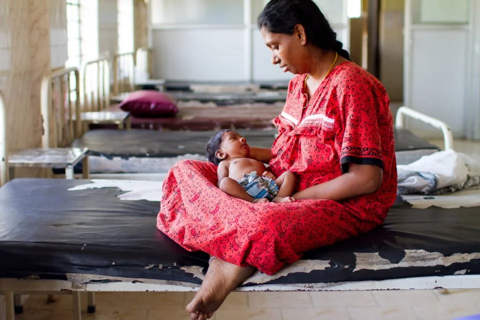 A mother holding her newborn baby at a maternal health clinic, representing the global health programs Lulan Studio helps fund