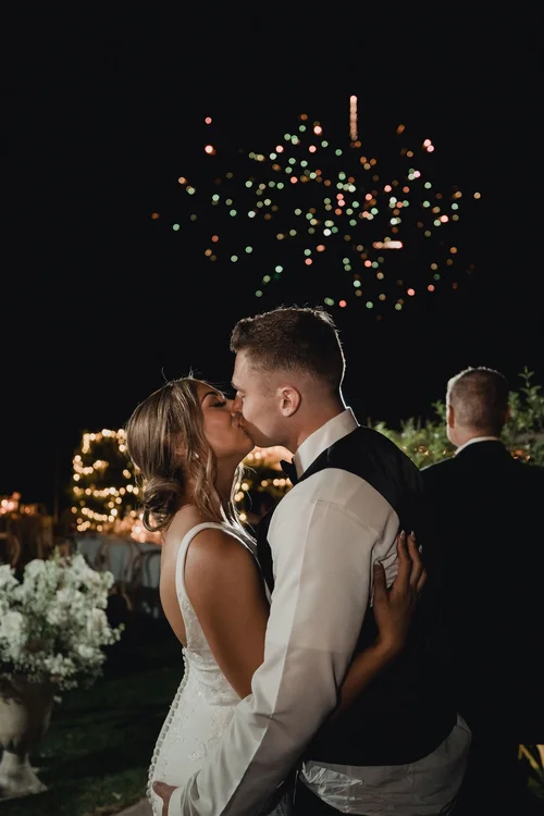 Bride and groom kissing on the dance floor at night as confetti bursts above them