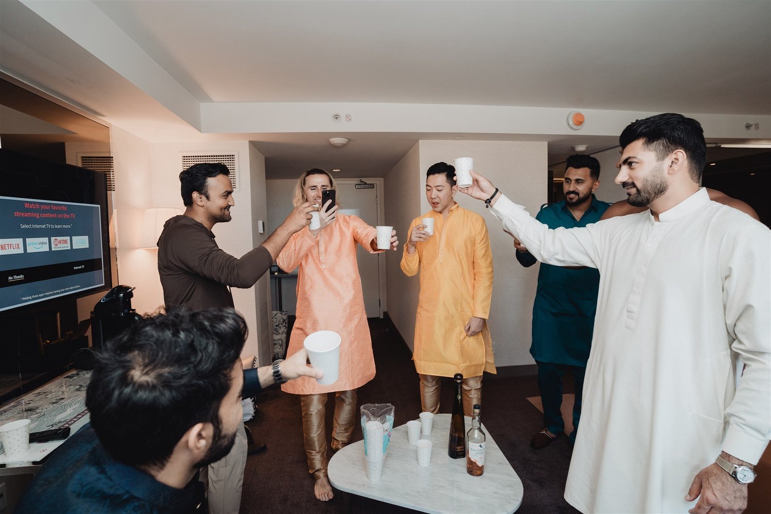 Groom and groomsmen in kurtas raising a celebratory toast in a hotel suite before the wedding