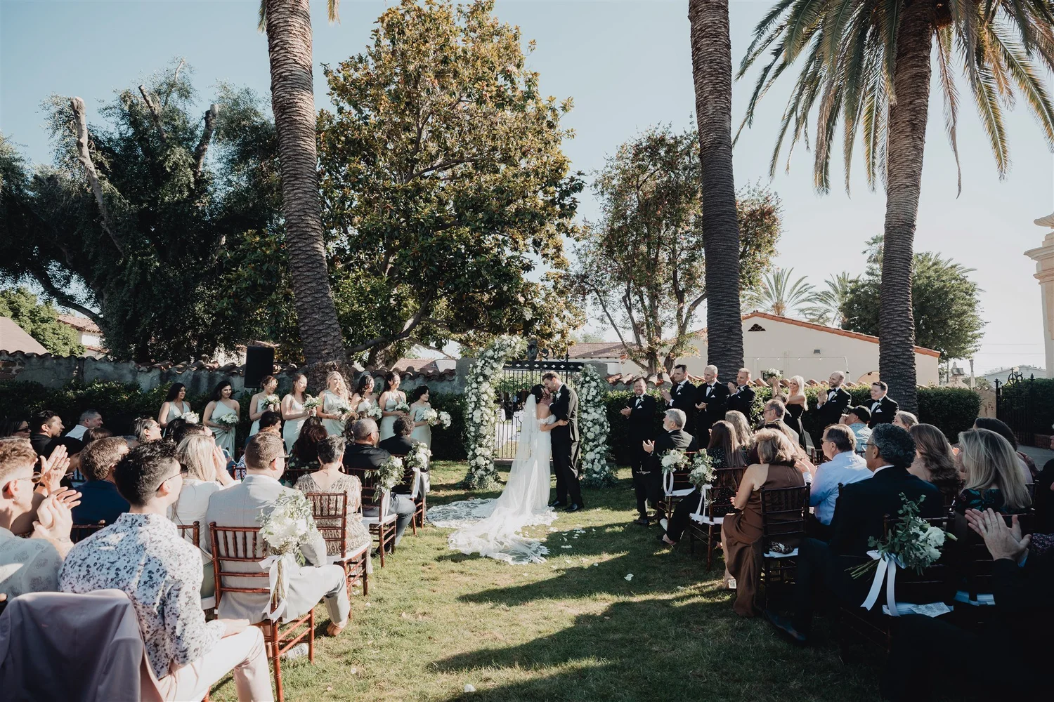 Garden ceremony under palms with guests seated on the lawn at Grapevine Arbor