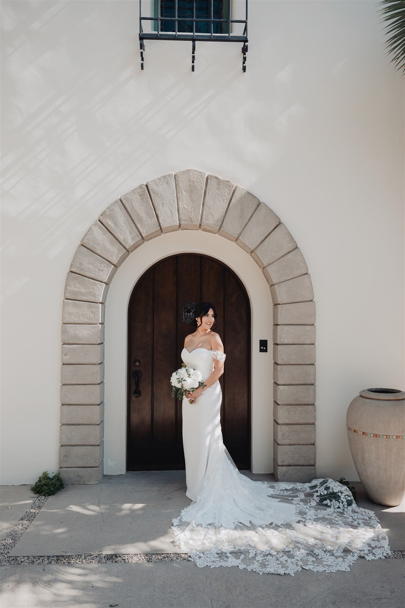Bride in front of a carved arched door in a white stucco wall, San Gabriel