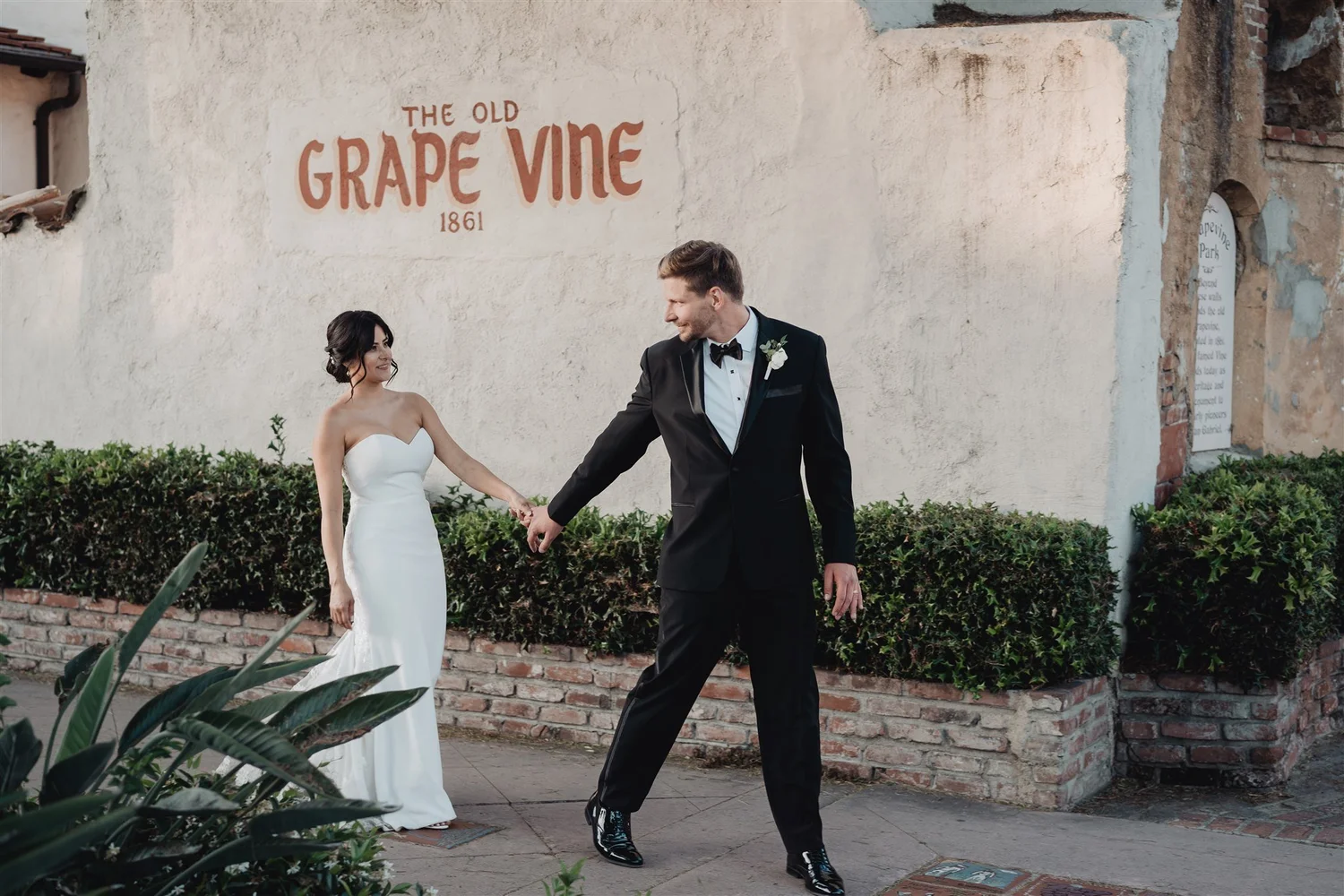 Couple walking past The Old Grape Vine sign painted on a white wall in San Gabriel