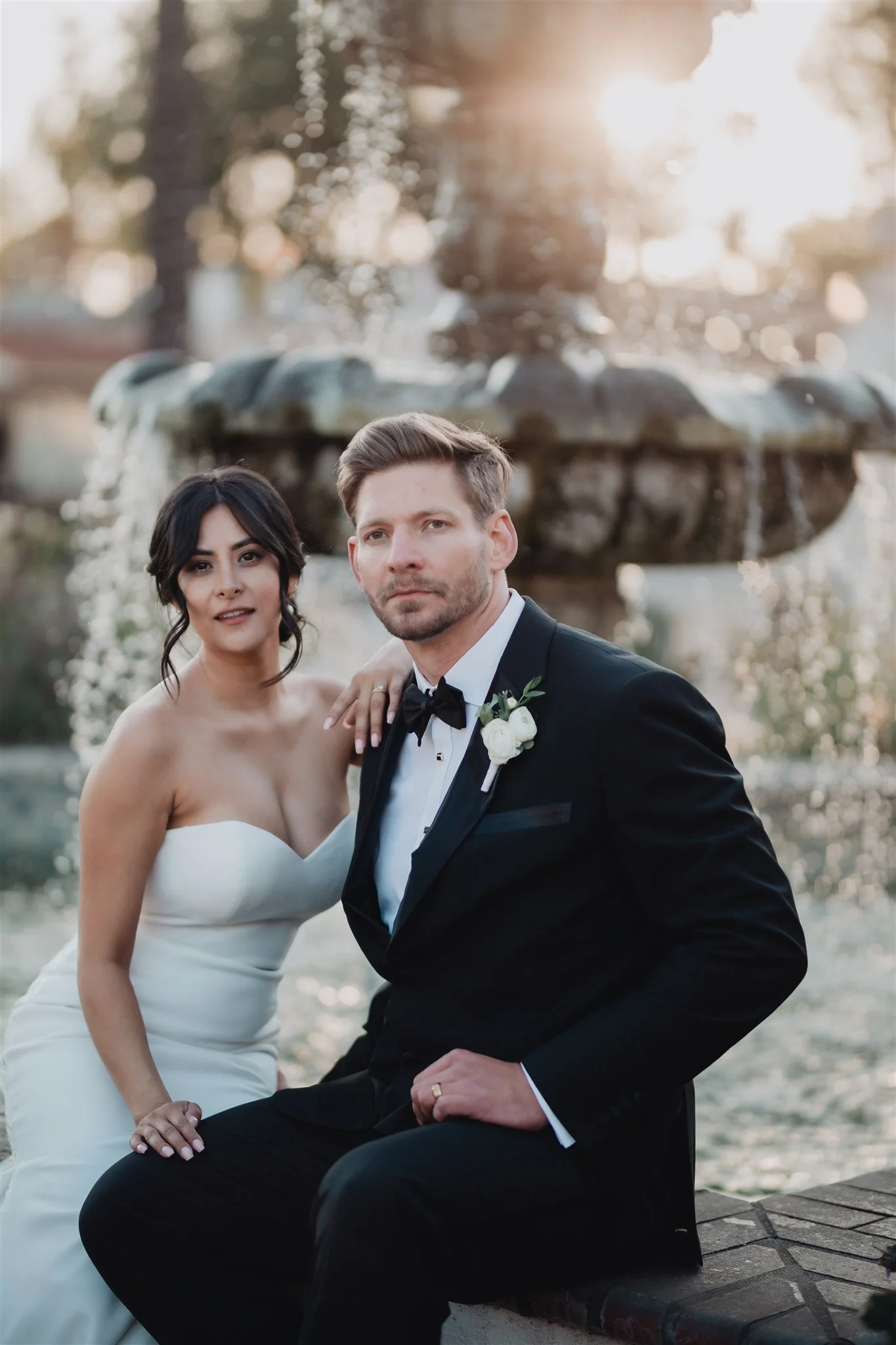 Couple sitting by a tiered stone fountain in golden light, San Gabriel