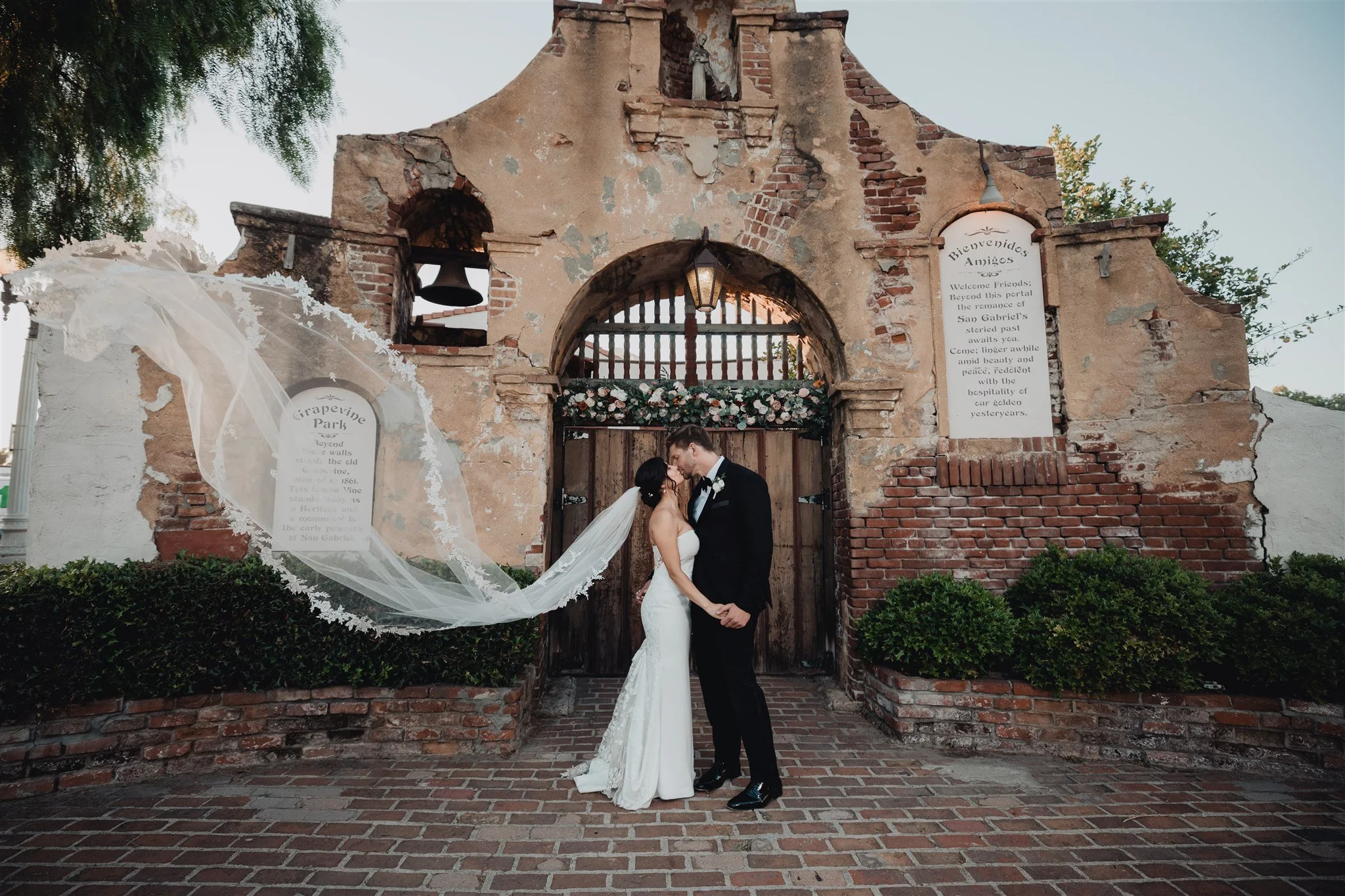 Long veil sweeping across the brick walk in front of the old mission-style arched wall at Grapevine Arbor in San Gabriel