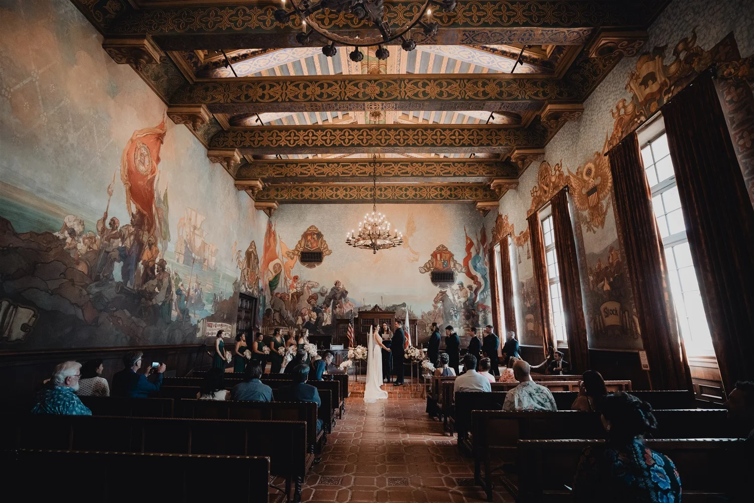 A wedding ceremony beneath a painted timber ceiling in a historic hall