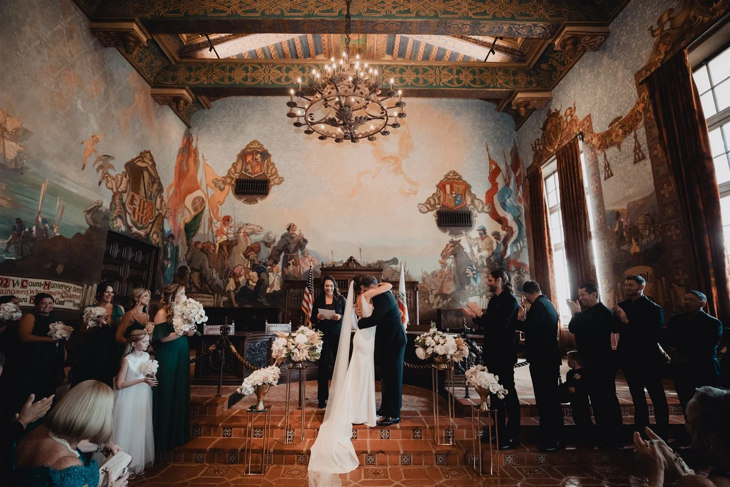 Bride and groom exchanging vows beneath the chandelier at the front of the Santa Barbara Courthouse Mural Room