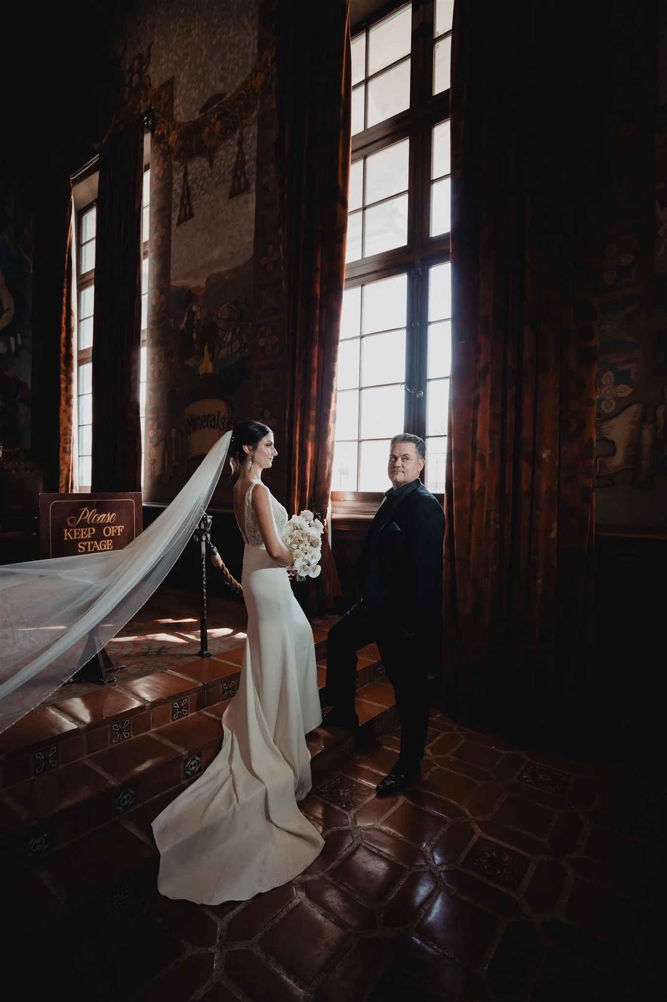 Bride with a long cathedral veil beside the tall arched windows of the Santa Barbara Courthouse