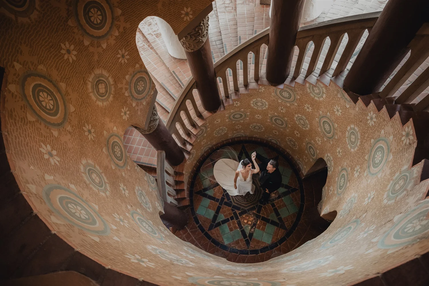 Overhead view of the couple standing at the foot of the painted spiral staircase inside the Santa Barbara County Courthouse