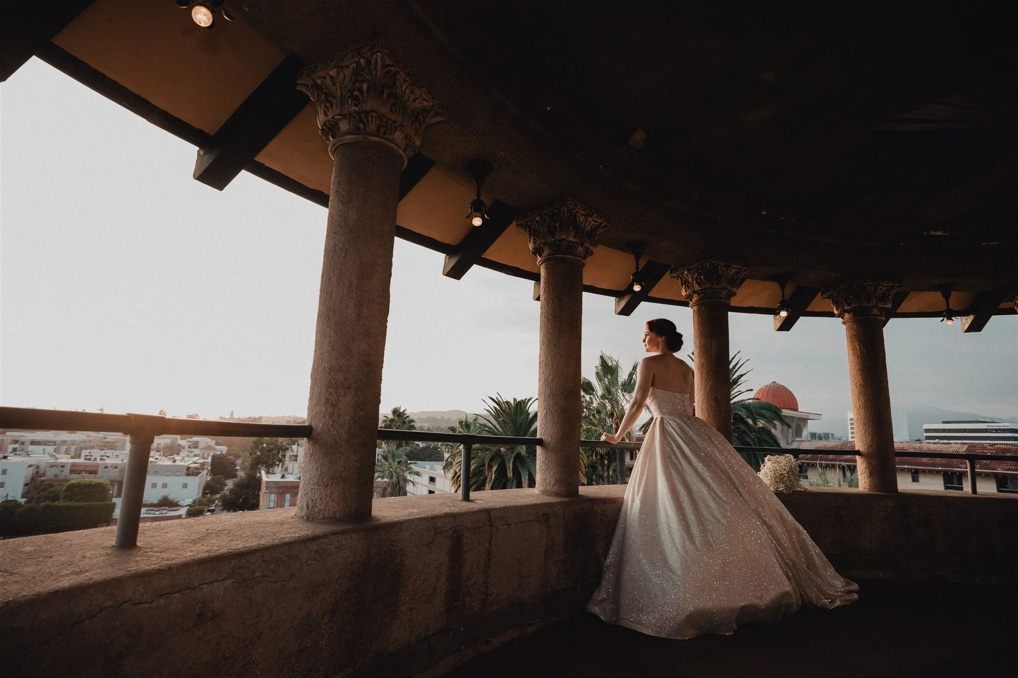 Bride on the rooftop terrace at Castle Green, framed by stone columns, with Pasadena beyond