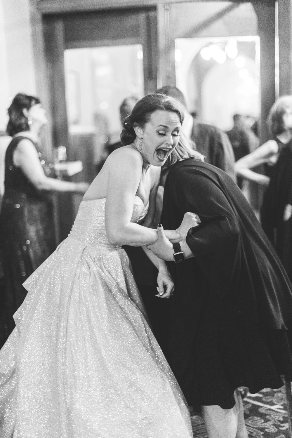 Bride laughing mid-dance with a guest on the reception floor, black and white