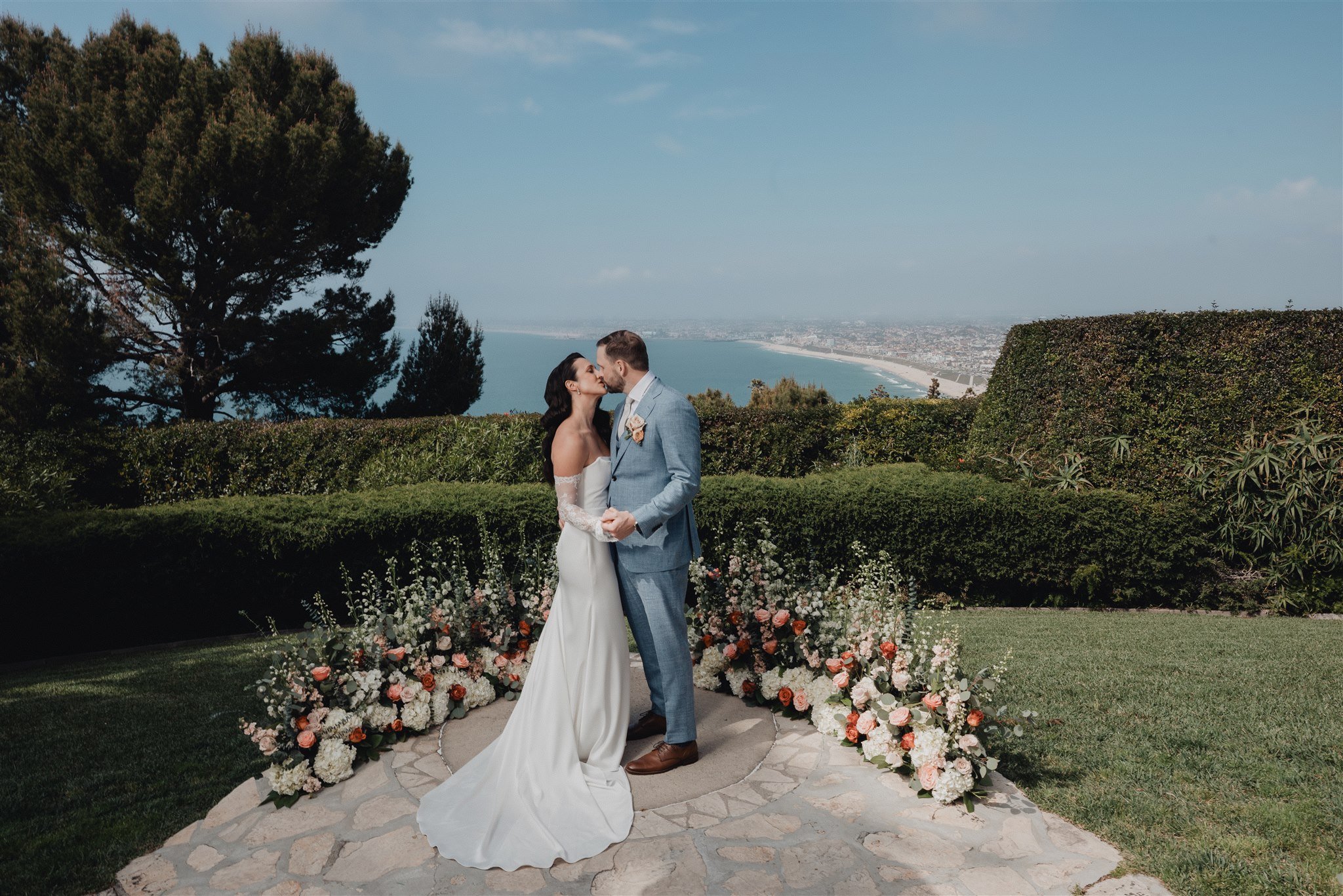 Couple kissing on the stone ceremony circle at La Venta Inn, Santa Monica Bay and the coastline behind them