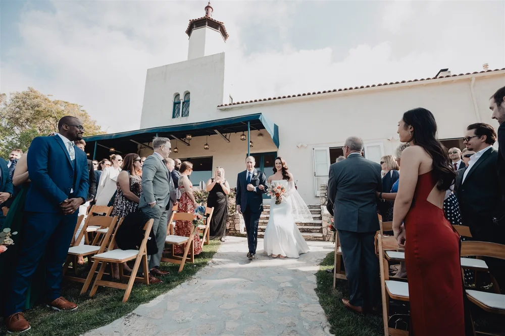 Bride walking down the aisle on the La Venta Inn lawn with the tower behind her