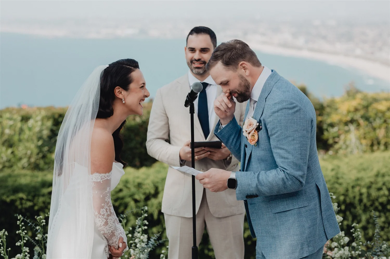Couple laughing during their ceremony on a coastal lawn at La Venta Inn, the officiant reading beside them