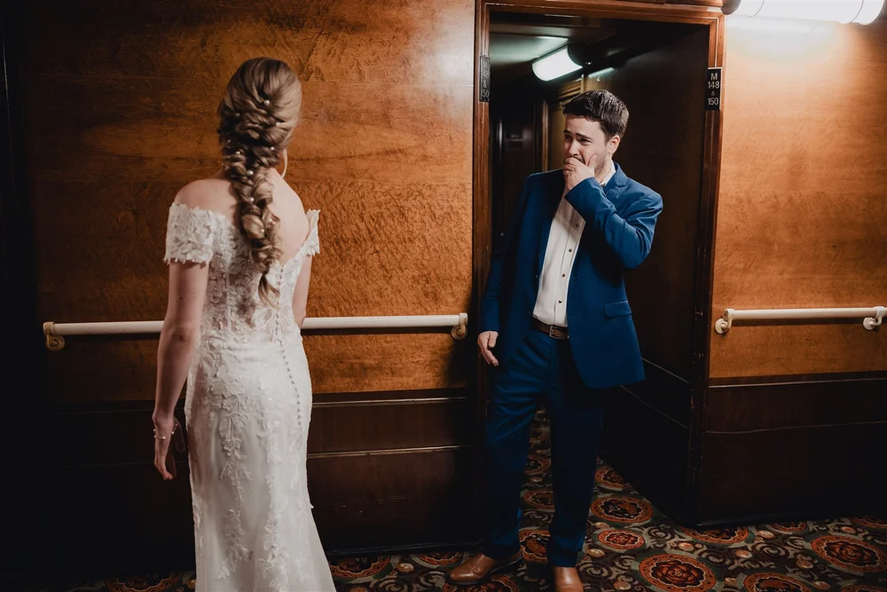 Bride in a braided updo in a wood-panelled Queen Mary corridor as the groom laughs in a blue suit