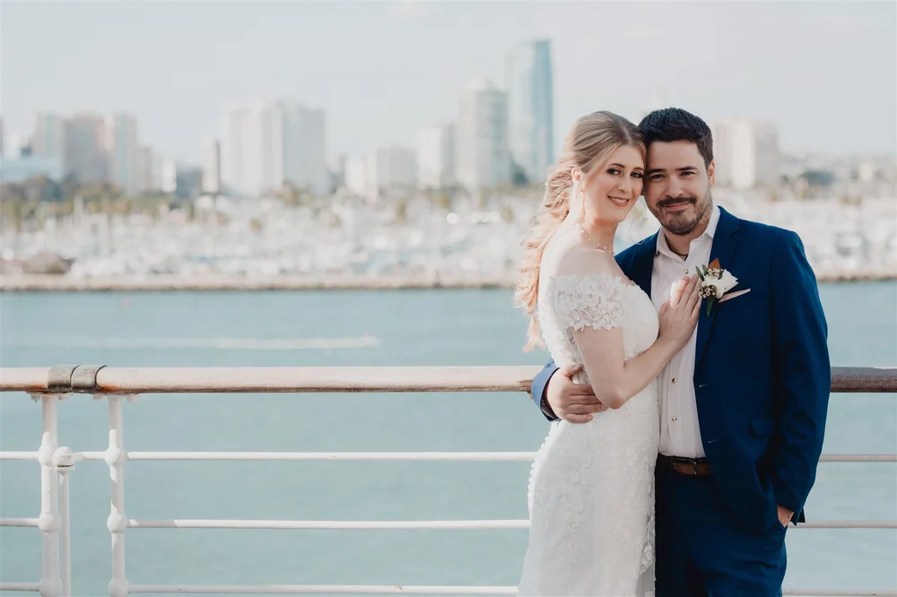 Bride and groom at the ship’s rail with the Long Beach skyline and marina behind them