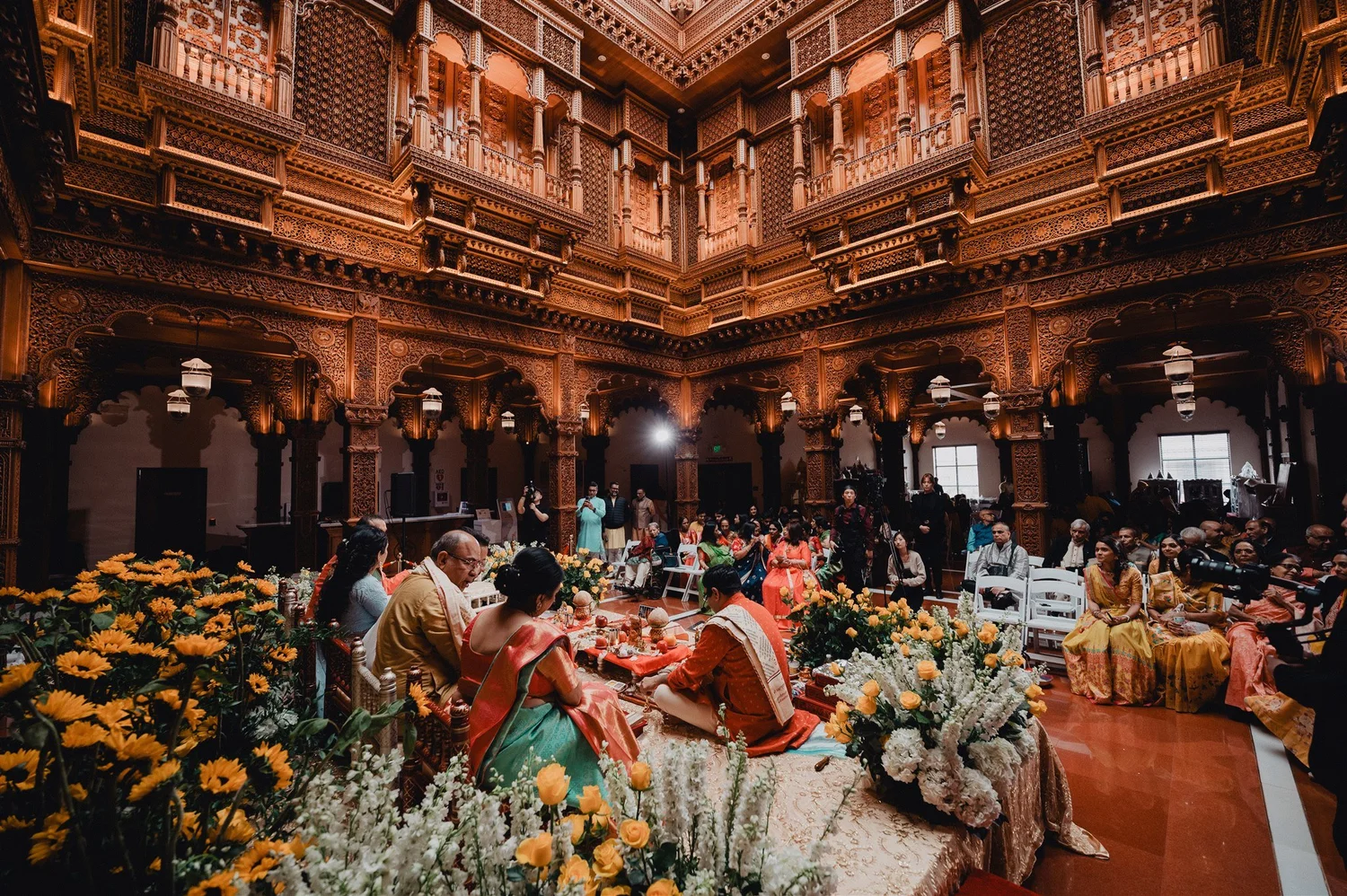 Family puja in a carved wooden hall lit by a skylight at the Chino Hills mandir