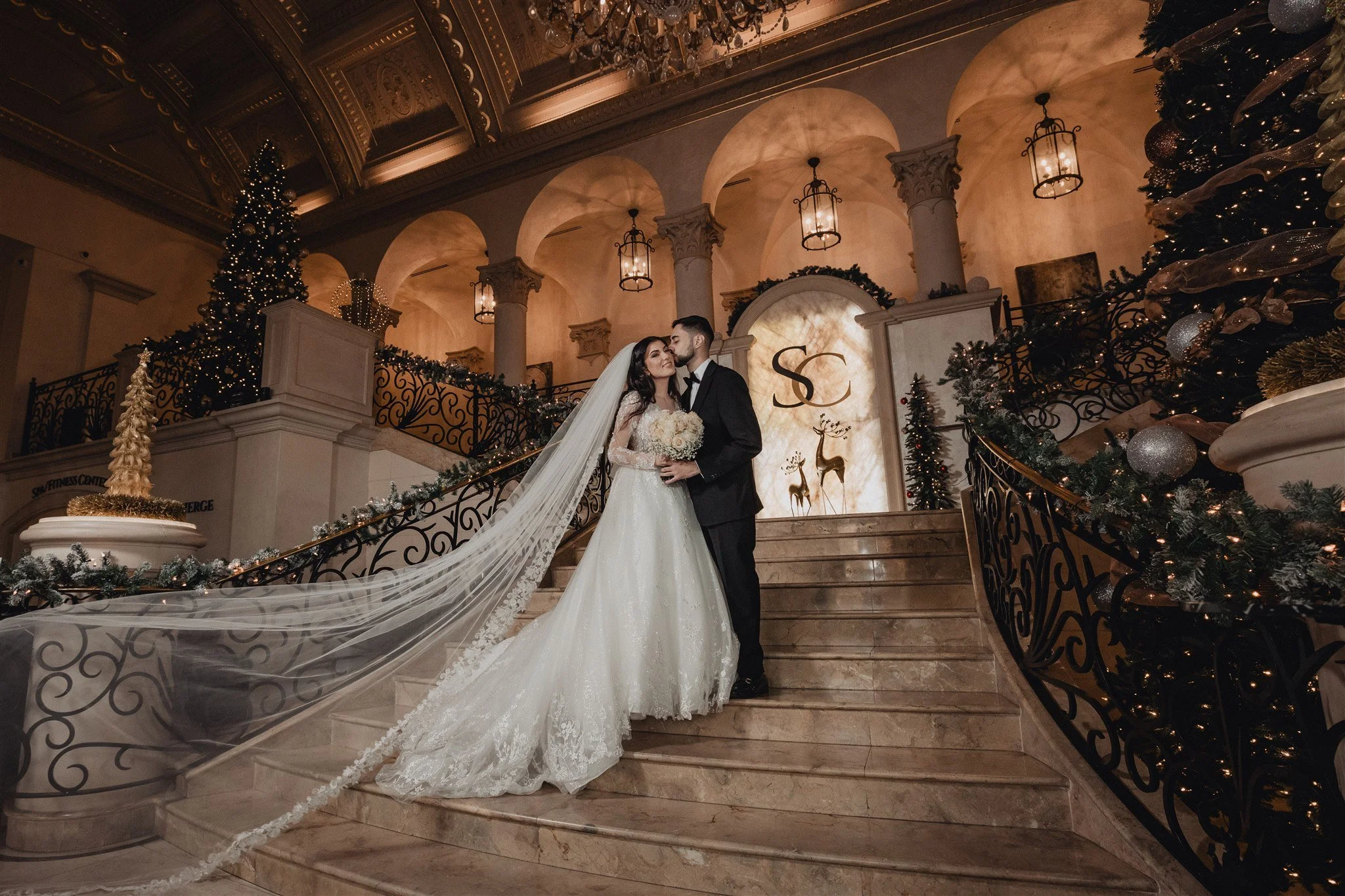 Bride and groom on the grand curved staircase at The Stirling Club in Las Vegas, her long veil across the steps