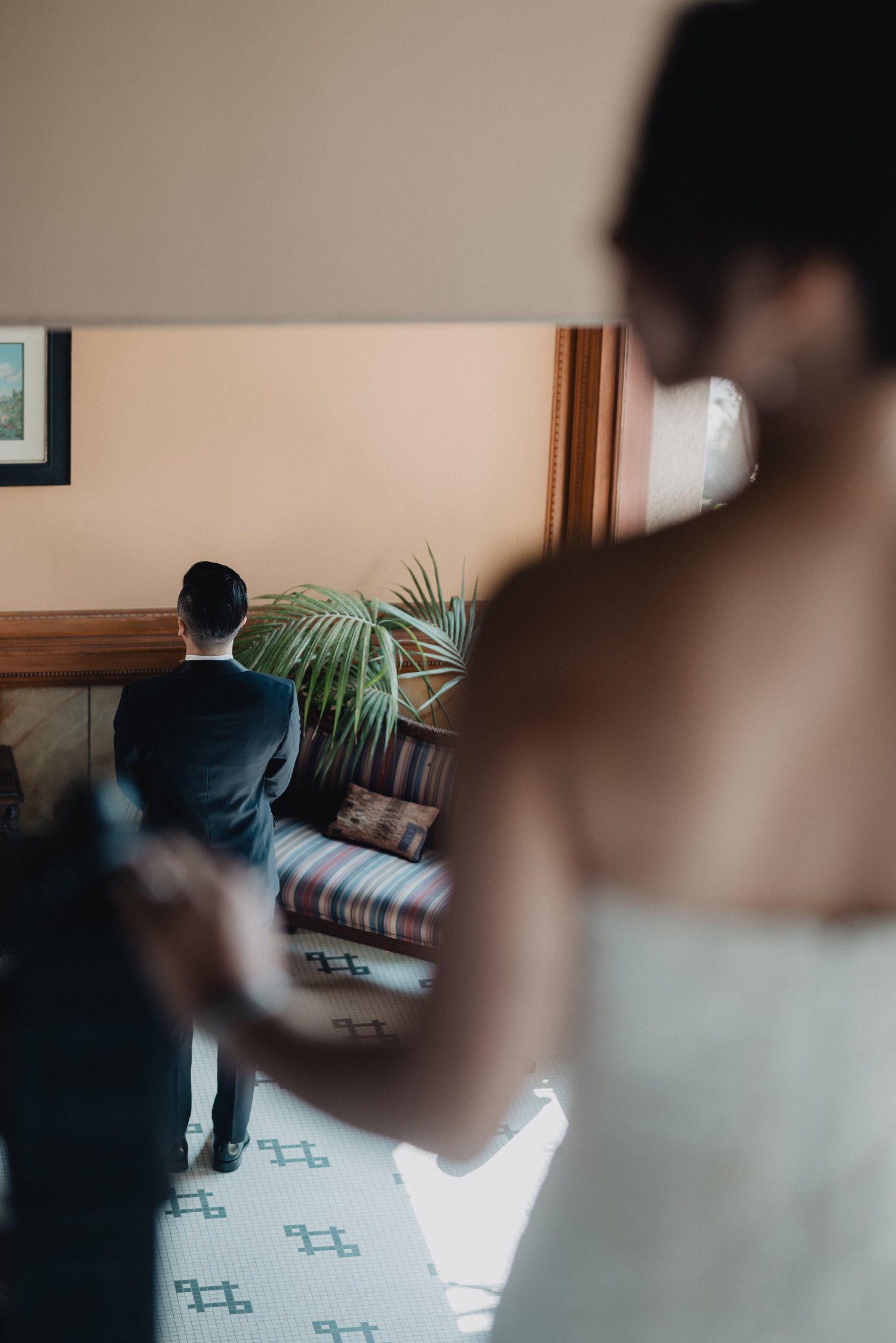 Over-the-shoulder view of a bride about to tap the waiting groom for their first look