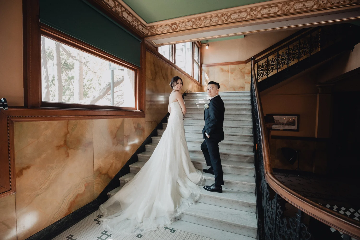 Couple on the grand wood-paneled staircase at Castle Green, lit by tall windows